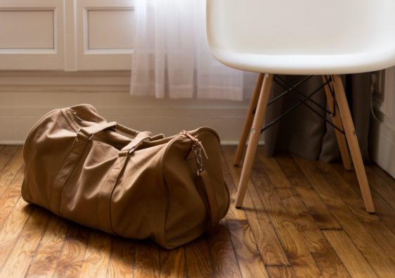 brown duffel bag beside white and brown wooden chair