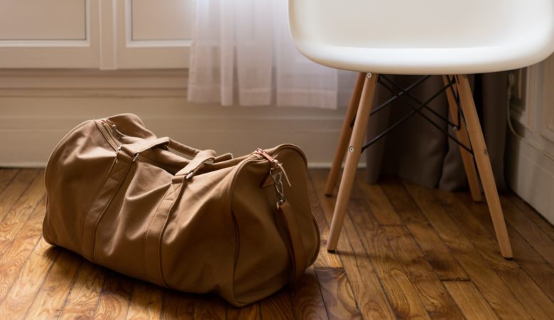 brown duffel bag beside white and brown wooden chair